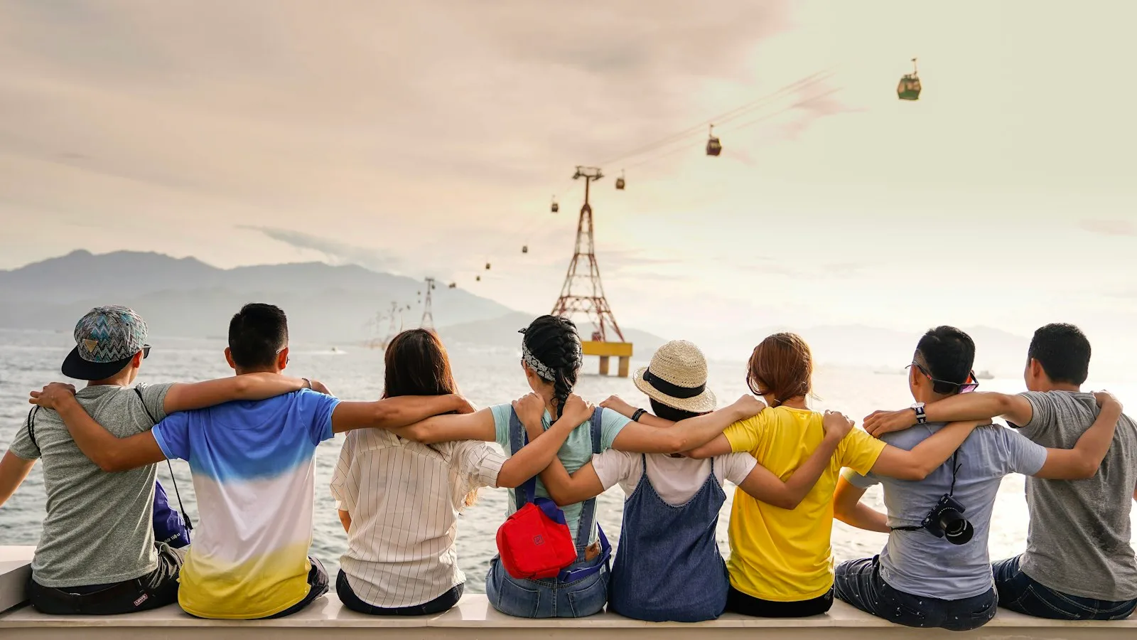 Junge Leute sitzen Arm in Arm am Meer und blicken in die Zukunft